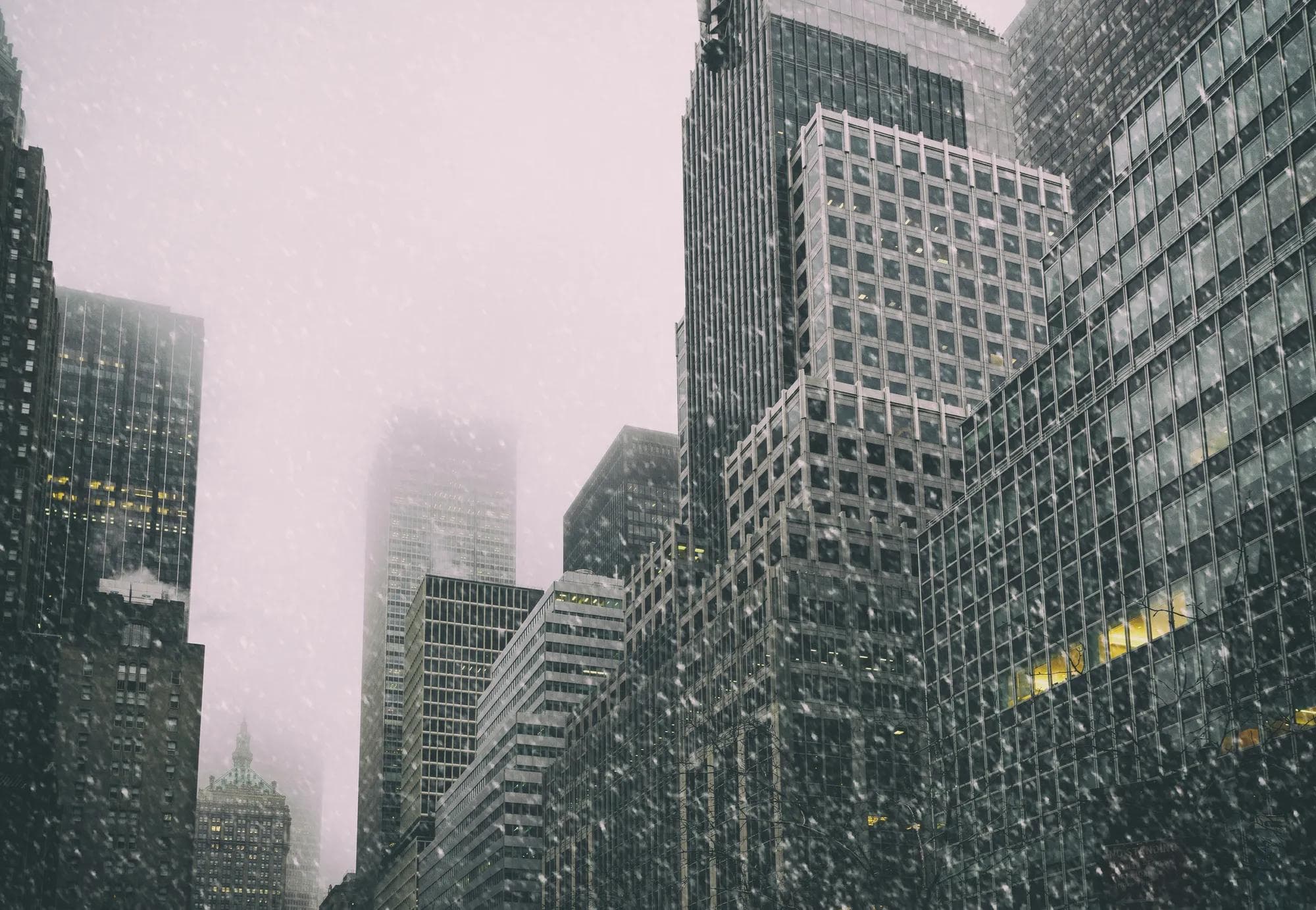 Snow falls on buildings in Manhattan during winter.   