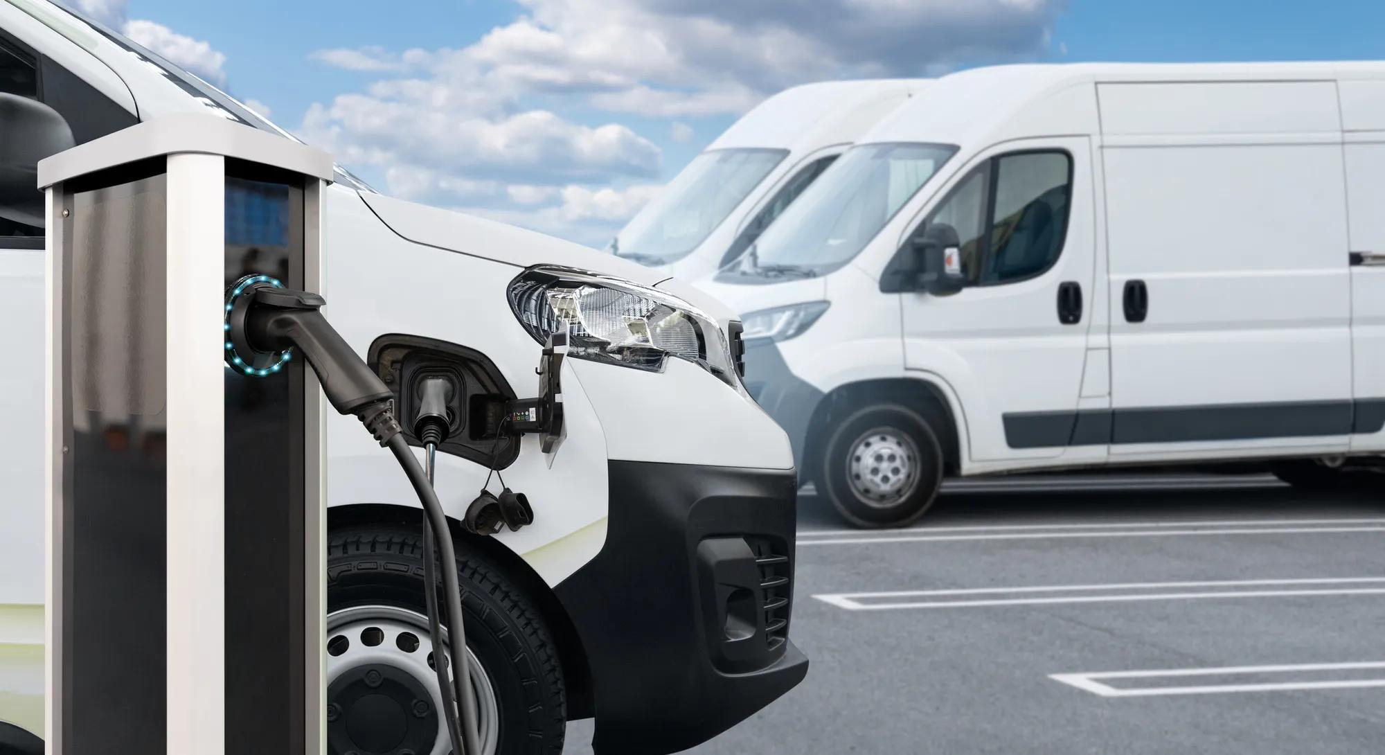 Electric delivery van with other electric vehicles at a charging station. 