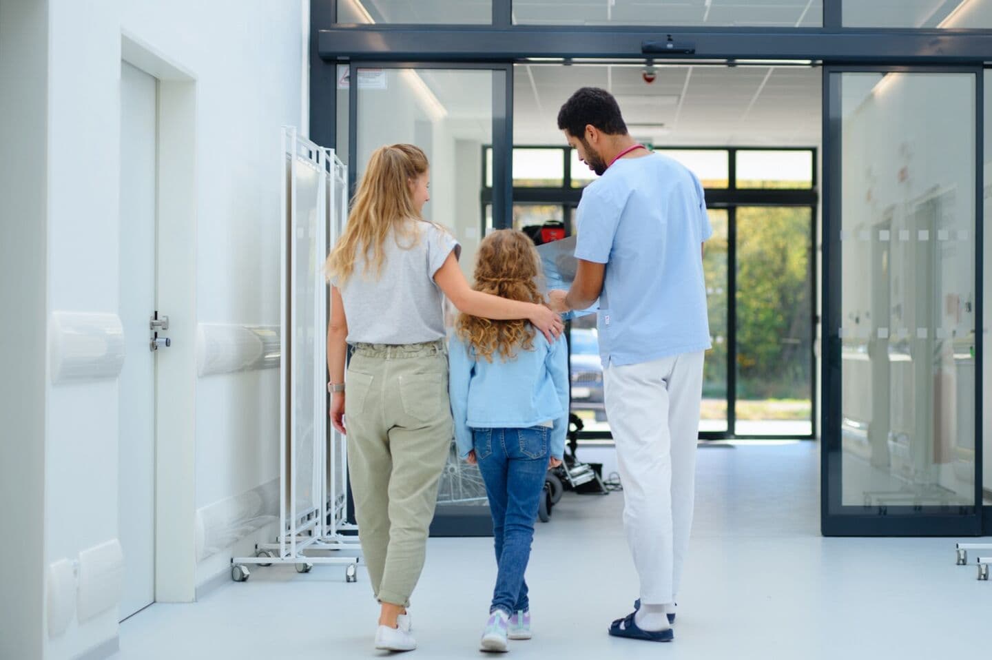 Rear view of a young doctor talking with mother and little girl at hospital corridor.