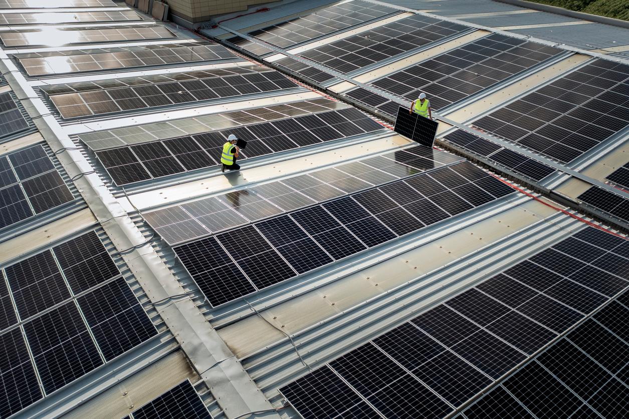 équipe d'ingénieurs utilisant la technologie lors de l'installation de panneaux solaires sur le toit d'un entrepôt