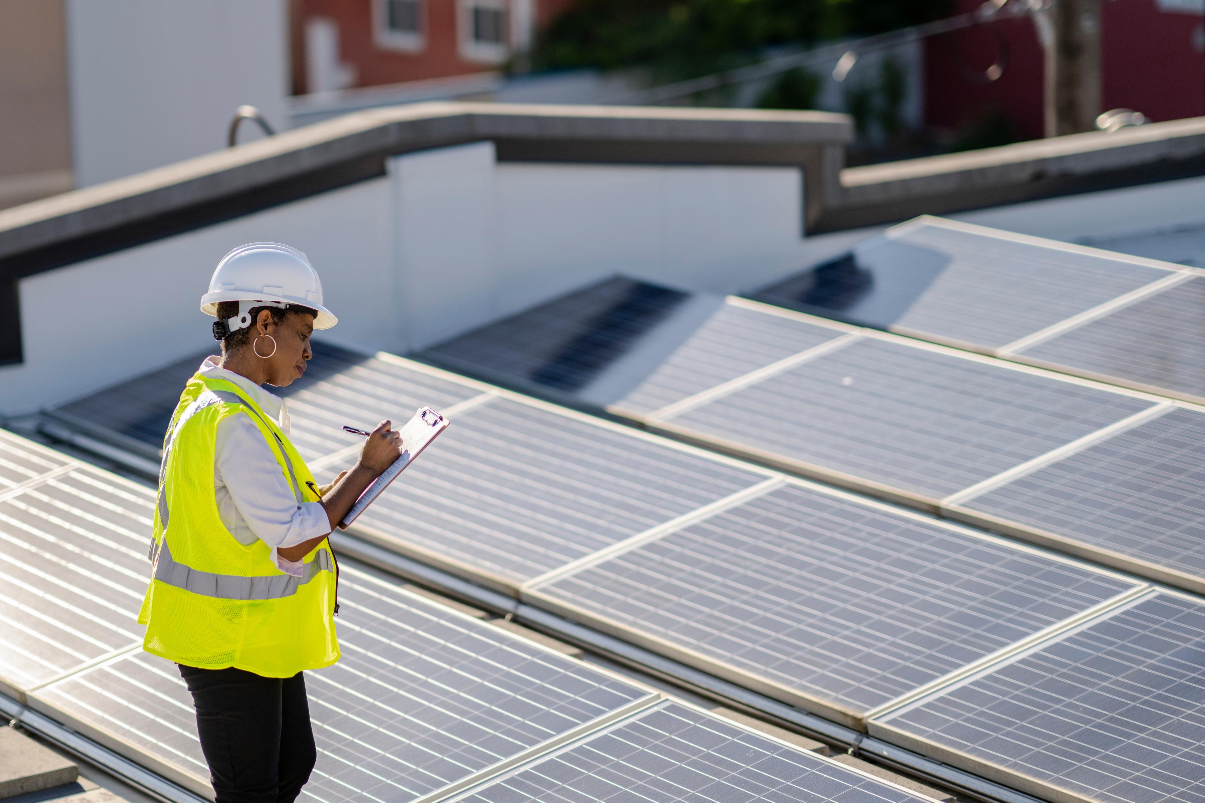 Une femme examine des panneaux solaires sur un toit pour en vérifier l’efficacité et le bon fonctionnement.