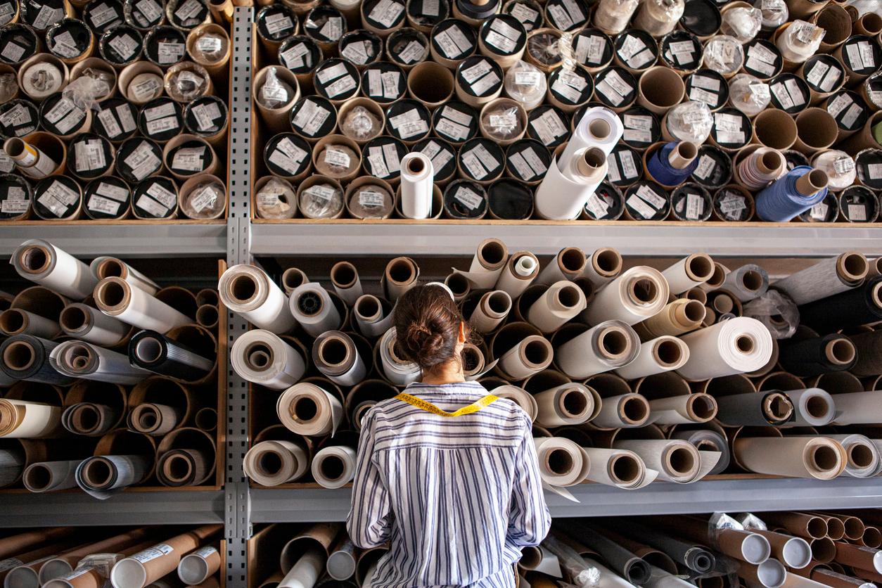 textile designer choosing fabric from stack of rolls inside sustainable workshop